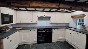 Una cocina con armarios blancos, estufa negra y piso de piedra.