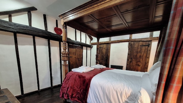 Una habitación tradicional con cama con dosel, paredes de madera y colcha roja.