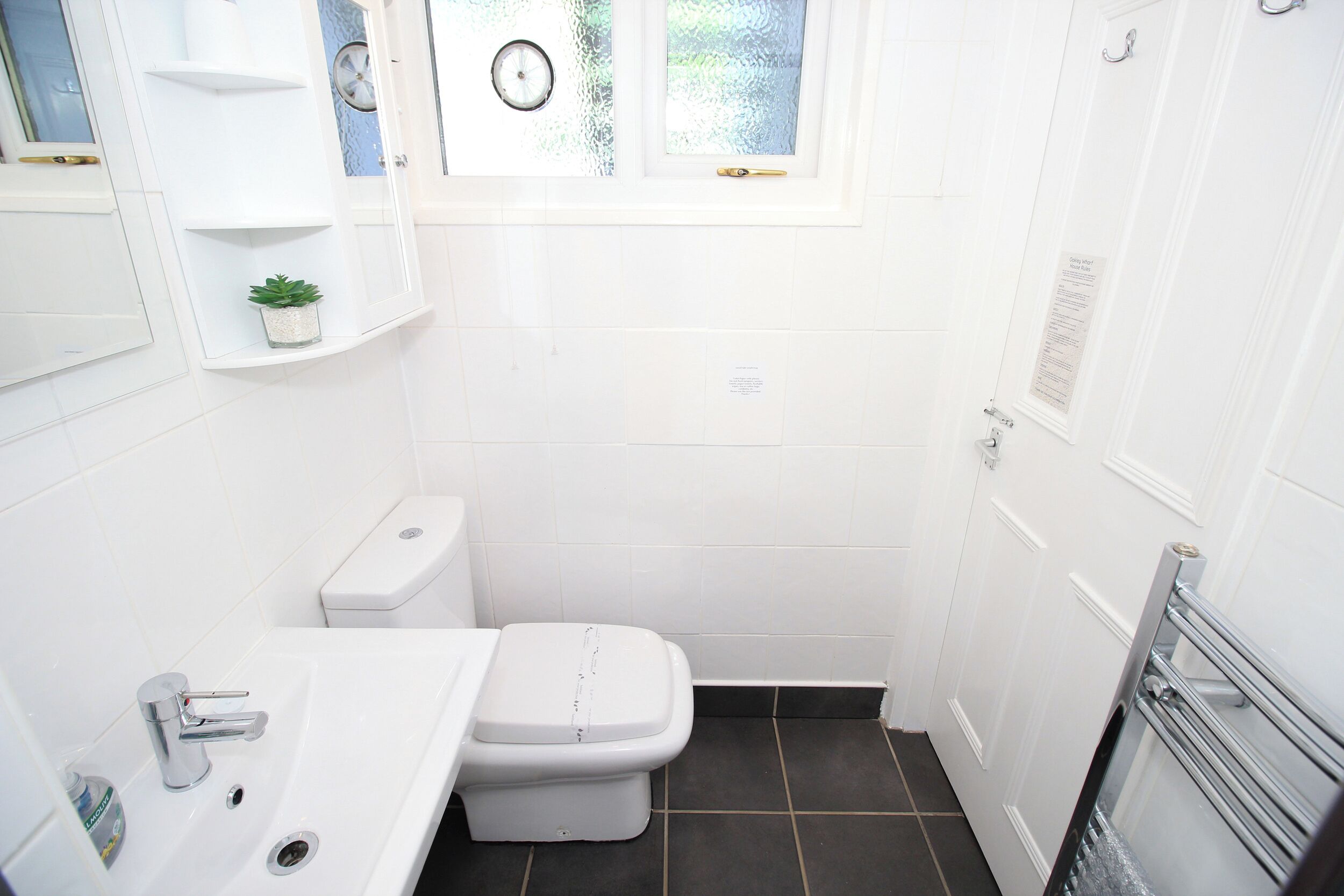 Ein kleines, weißes Badezimmer mit Toilette, Waschbecken und einem Fenster über der Toilette.