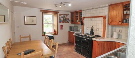 A compact kitchen with a dining table, wooden chairs, a stove, a microwave, and a window.