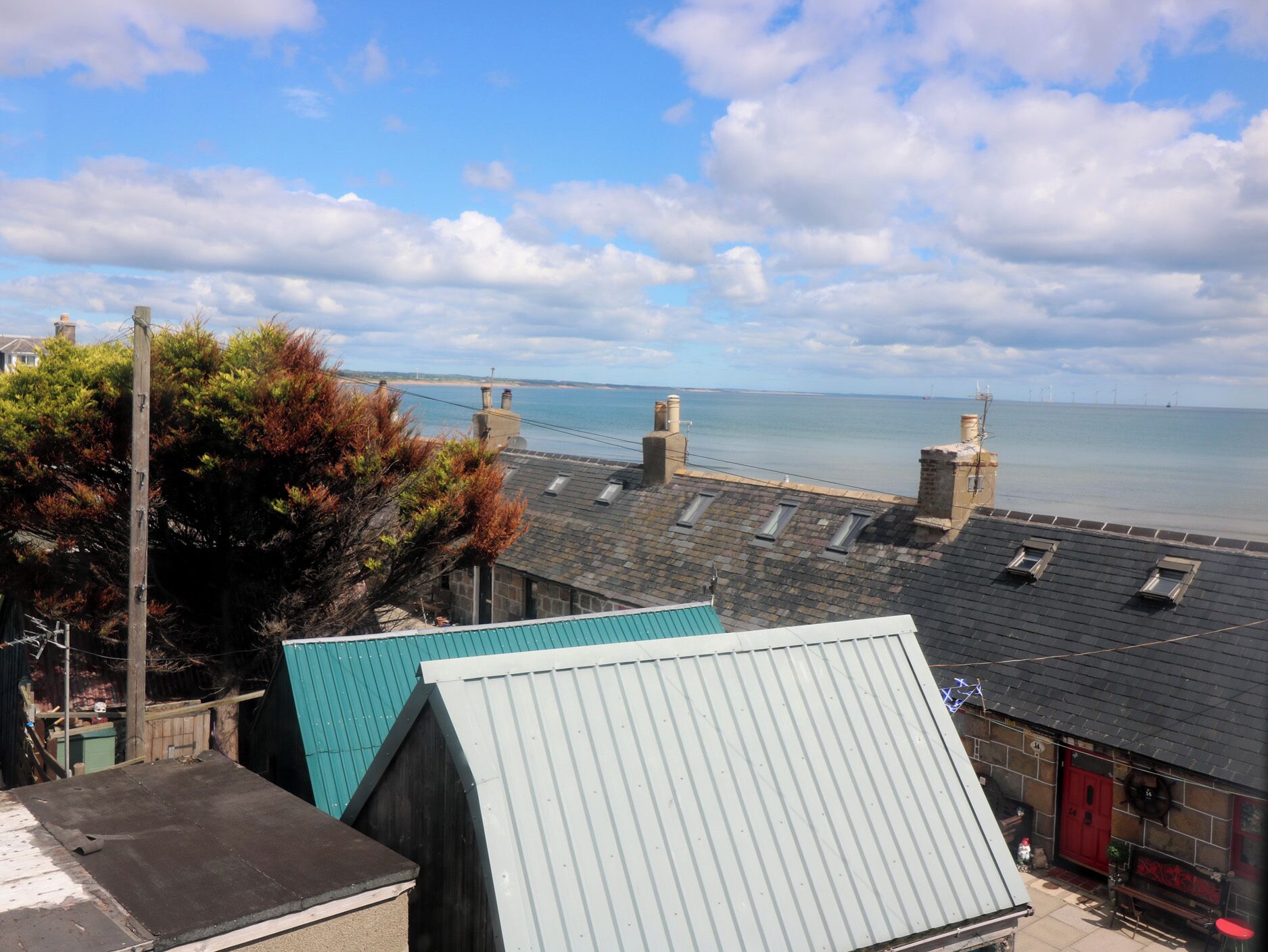 A coastal view with a clear sky, a sea, and a row of buildings with a prominent chimney.