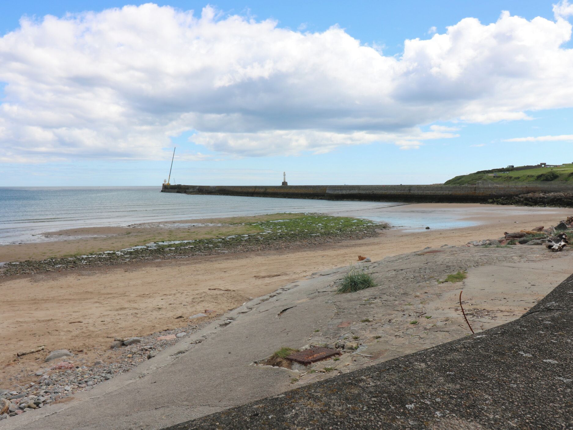 A coastal landscape with a sandy beach, a rocky shoreline, and a long pier extending into the water.