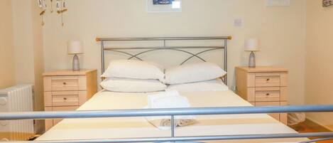 A neatly made bed with white linens, two bedside tables with lamps, and a radiator on the left.
