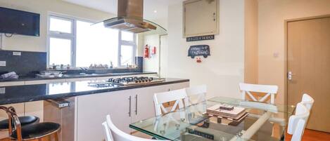 Una cocina moderna con una isla central, muebles blancos y una mesa de comedor de vidrio con sillas blancas.