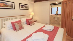 A neatly made bed with white and red bedding, a red throw blanket, and a folded white towel on the bed. - Jasmine Cottage (Keswick)