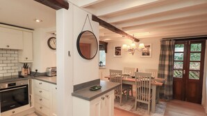 A modern kitchen with white cabinets, a Bosch oven, and a dining area with wooden chairs and a table. - Jasmine Cottage (Keswick)
