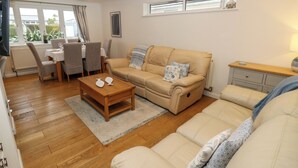 A modern living room with a beige sofa, a wooden coffee table, and a dining area with a table and chairs. - Seafarer's Rest (Chichester)