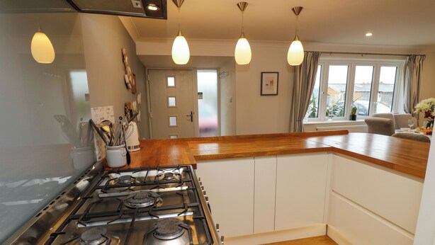 A modern kitchen with a gas stove, wooden countertop, pendant lights, and a view of the outdoors through a window. - Seafarer's Rest (Chichester)