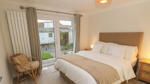 A bedroom with a large bed, a chair, a nightstand, and a view through a sliding glass door to the outside. - Seafarer's Rest (Chichester)