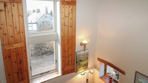 Ein Zimmer mit Holzhörnern, einem Fenster mit Blick auf ein Steinhaus, einer Wandleuchte und einem gerahmten Bild.
