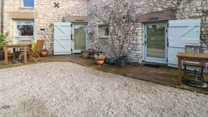 Ein Steinhaus mit zwei Türen, einem Kieshof und Gartenmöbeln.