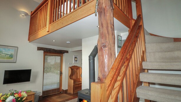 Ein Wohnzimmer mit einer Holztreppe, einem Kamin, einem Fernseher und einer Blumenkomposition.