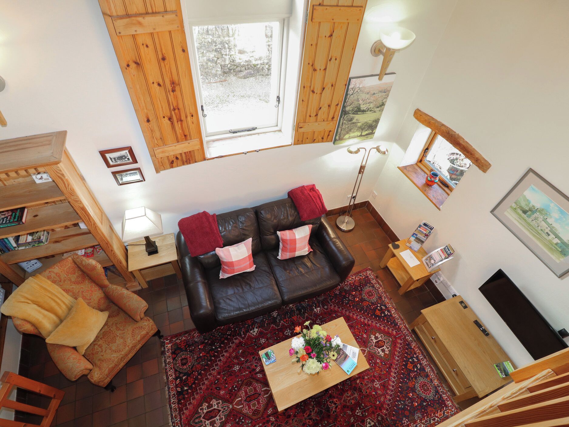 A cozy living room with a leather sofa, a wooden coffee table with a vase of flowers, a patterned rug, and a bookshelf.