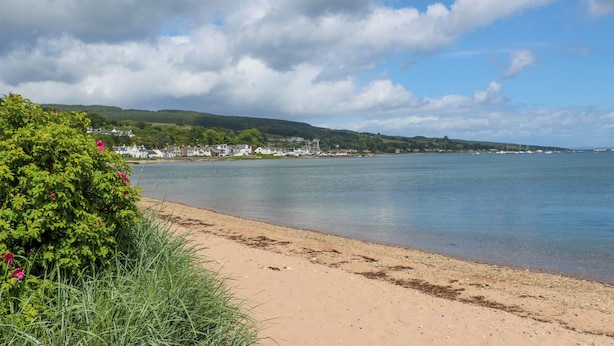 Un paysage côtier avec une plage de sable, une mer calme et une ville en arrière-plan.