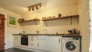 A kitchen with white cabinets, a built-in oven, a washing machine, and a shelf with kitchen utensils. - The Mytton at Mill Barn (Craven Arms)