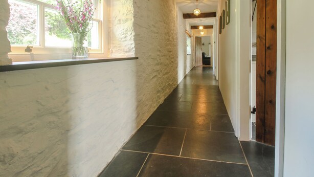 A hallway with stone walls, a wooden door, and a window with flowers. - The Mytton at Mill Barn (Craven Arms)