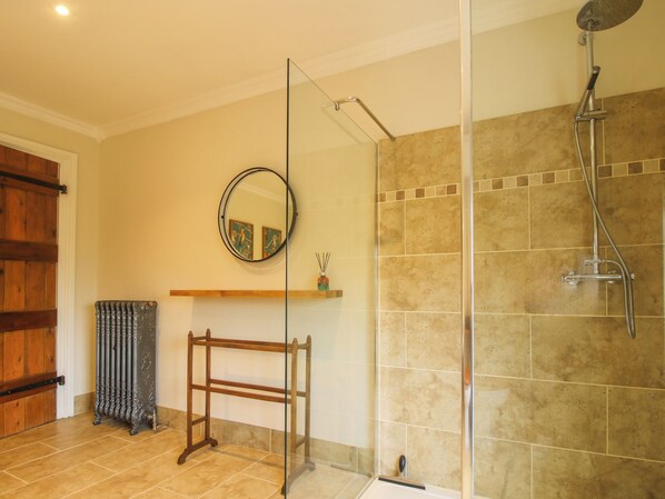 Un baño con cabina de ducha de vidrio, radiador de madera, espejo y repisa con objetos decorativos.