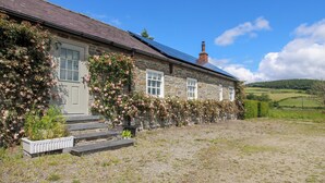 A stone house with a sloped roof, a chimney, and a garden with pink flowers. - The Mytton at Mill Barn (Craven Arms)