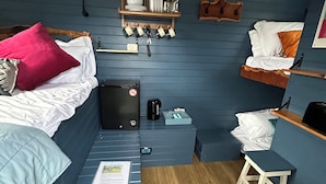 A compact room with two beds, a small kitchenette, and a wooden shelf with kitchen utensils. - Acres Meadow (Dorchester)