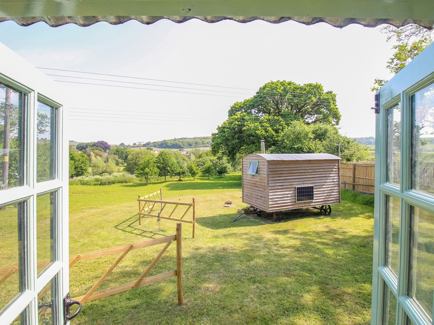 A wooden structure in a grassy yard with a view of a tree and hills in the background.