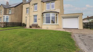 A two-story house with a front garden, a bench, and a garage. - Burnbank (Maryport)