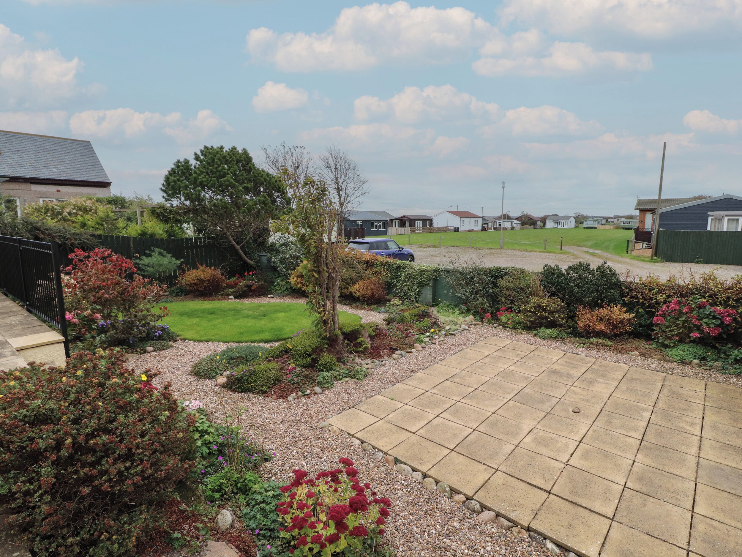 Ein privater Garten mit einer gepflasterten Terrasse, verschiedenen Sträuchern und einer Rasenfläche.