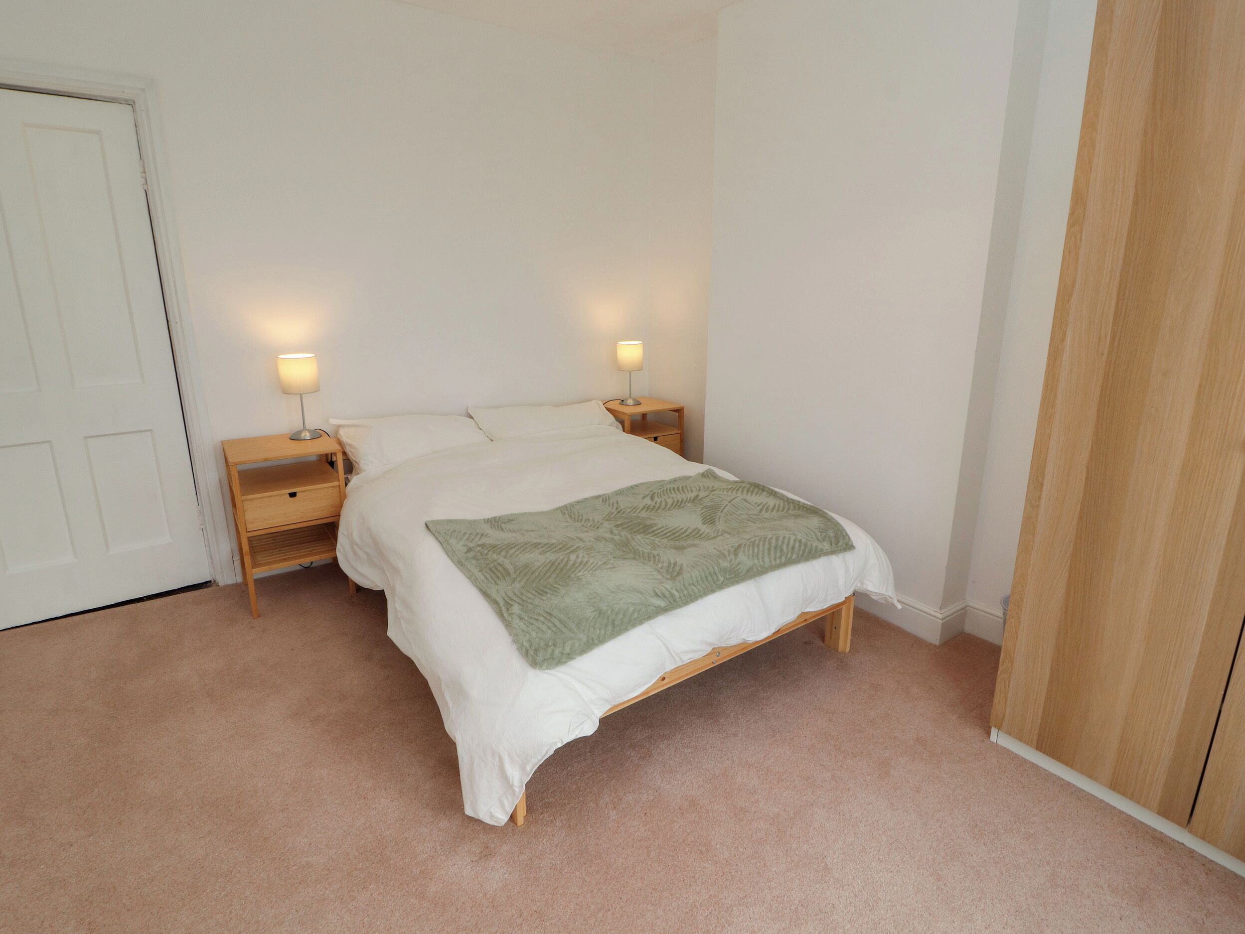 Une chambre à coucher avec un lit, deux tables de chevet avec des lampes, une armoire en bois et un sol recouvert d’une moquette.