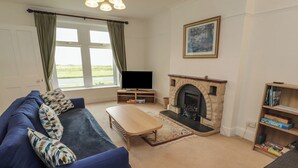 A living room with a blue sofa, a coffee table, a fireplace, a television, and a bookshelf. - Burnbank (Maryport)