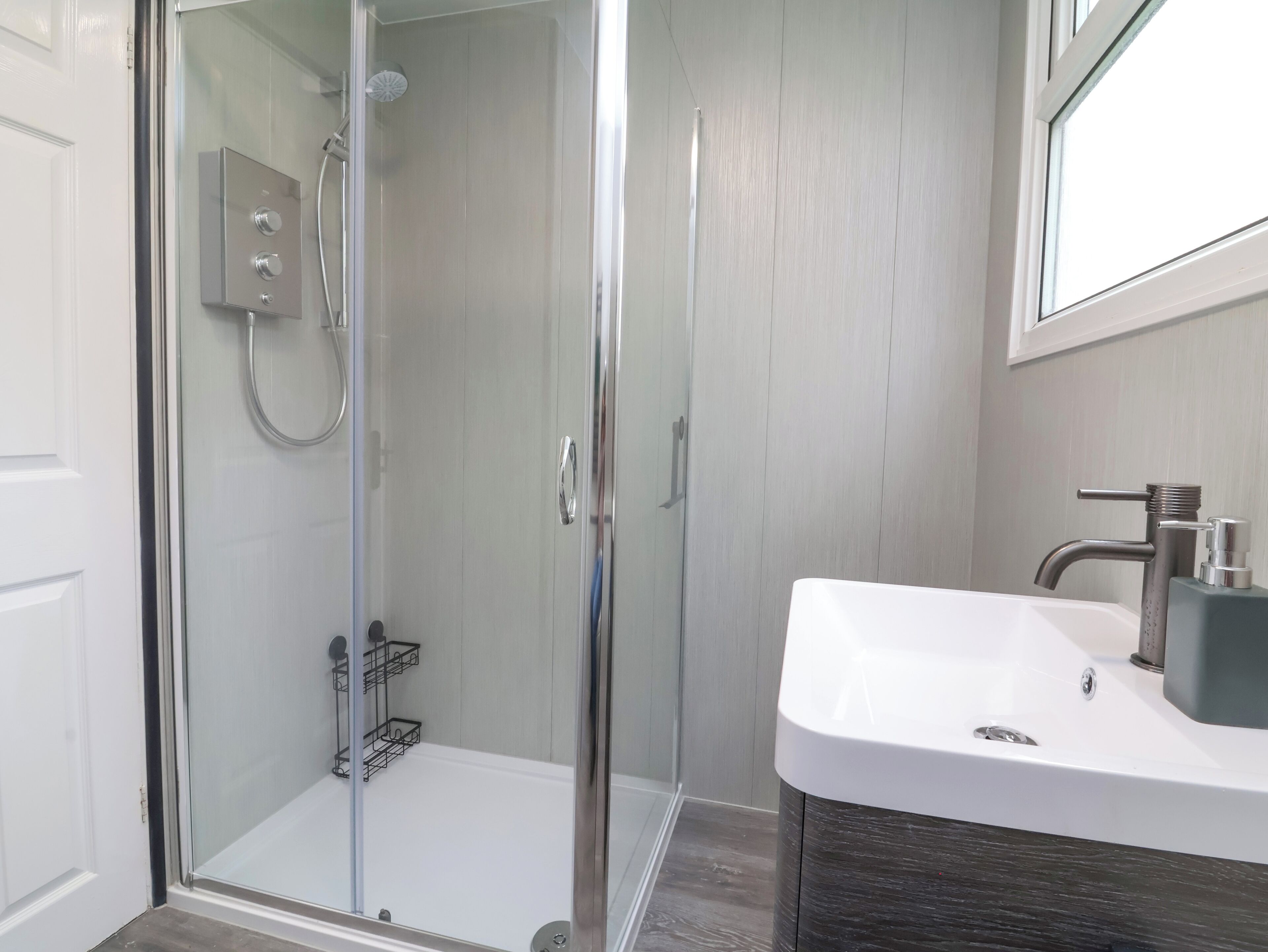 A modern bathroom with a glass-enclosed shower, a white sink, and a dark wood vanity.