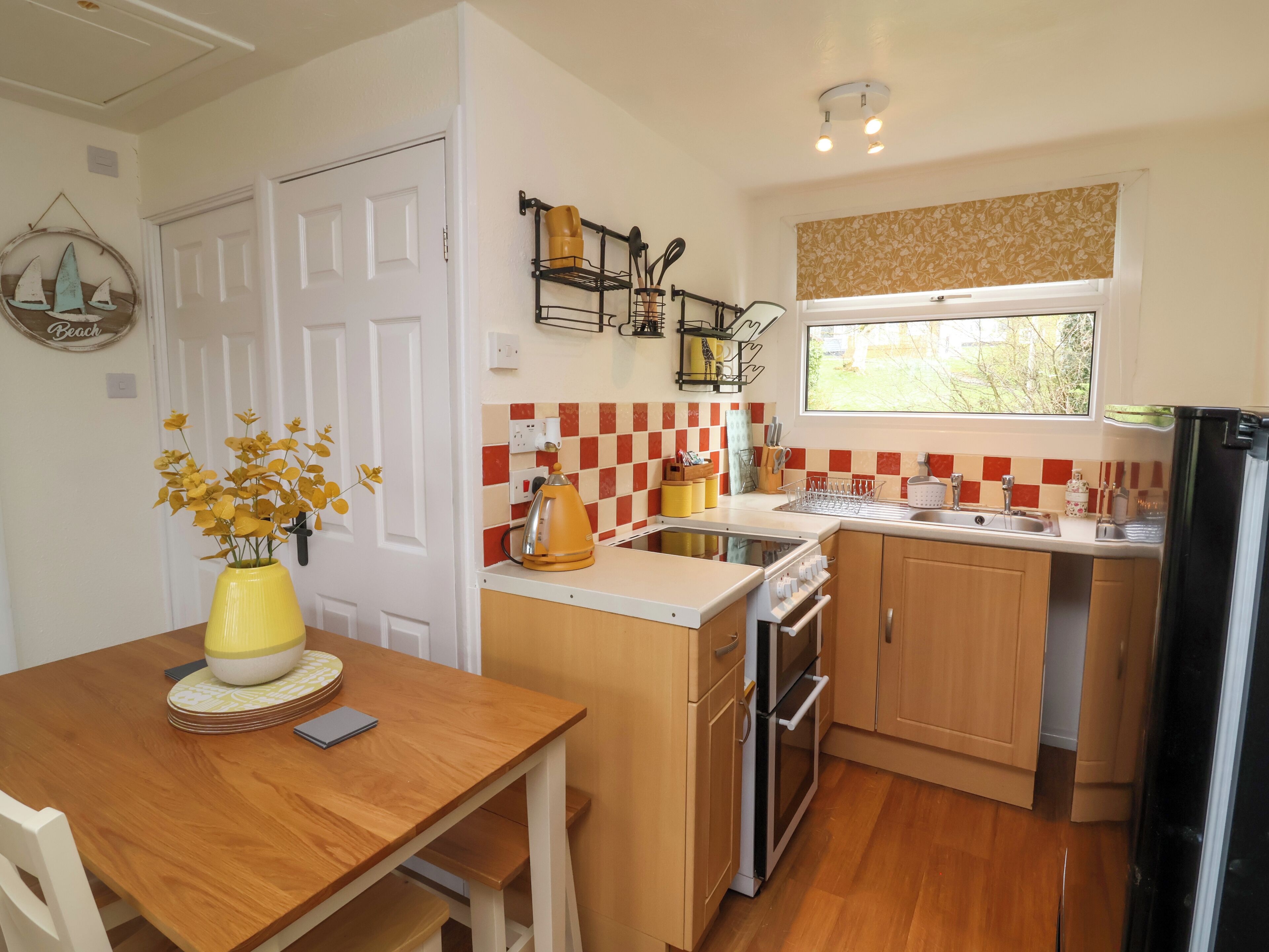A compact kitchen with wooden cabinets, a built-in oven, a sink, and a window with a view of greenery.