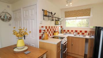 A compact kitchen with wooden cabinets, a built-in oven, a sink, and a window with a view of greenery.