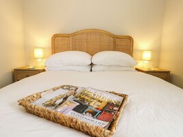 Una cama bien hecha con una revista encima, dos lámparas de noche y un cabecero de madera.