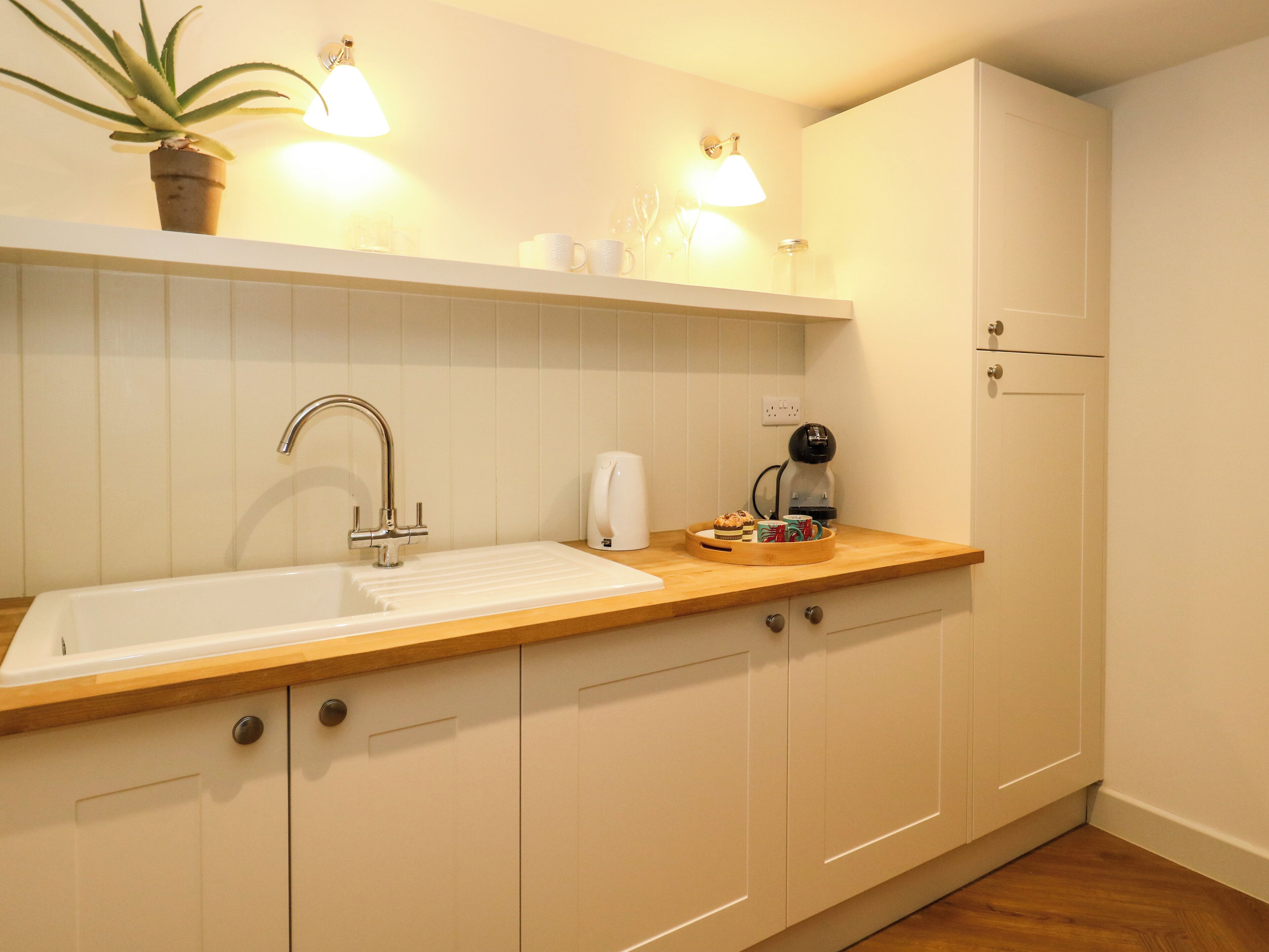 A kitchen with a white sink, wooden countertop, and cabinets. There is a plant on the countertop and a coffee maker on the counter.