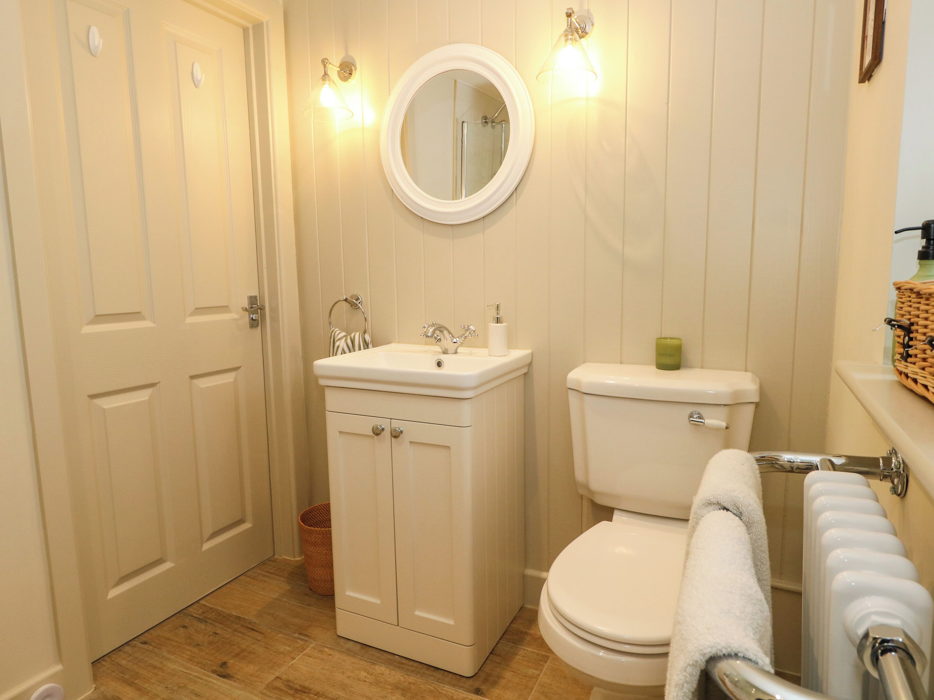 A bathroom with a white sink, toilet, and a mirror. There is a wicker basket on the floor and a towel rack with a towel.