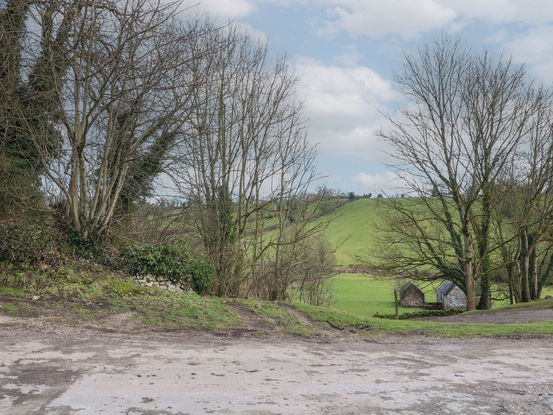 Un paysage rural avec un chemin de terre menant à un mur de pierres et à un petit bâtiment en pierre.