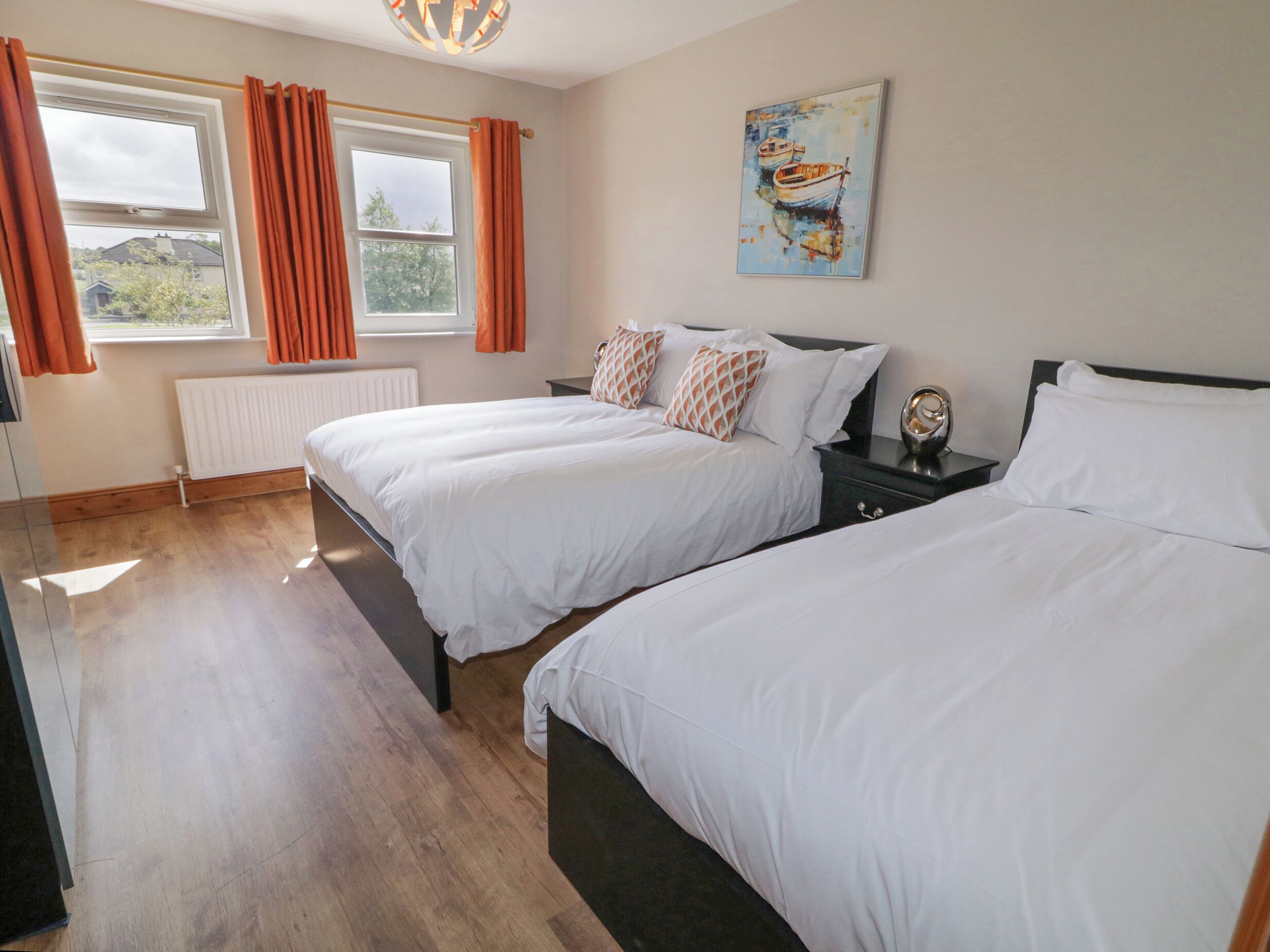 A hotel room with two single beds, a window with curtains, a radiator, and a painting on the wall.