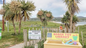 Une zone de plage avec des panneaux indiquant les activités sportives proposées par Adventure Sports Culdaff et une bibliothèque de jeux de plage.