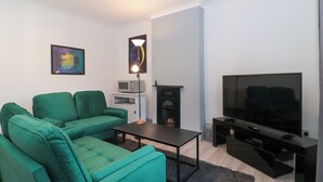A modern living room with a green sofa set, a flat-screen TV, a fireplace, and a microwave on a white cabinet. - Cosy Nest (Glastonbury)