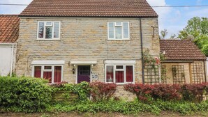 A stone house with a tiled roof, two windows with shutters, and a sign reading "COSY NEST". - Cosy Nest (Glastonbury)