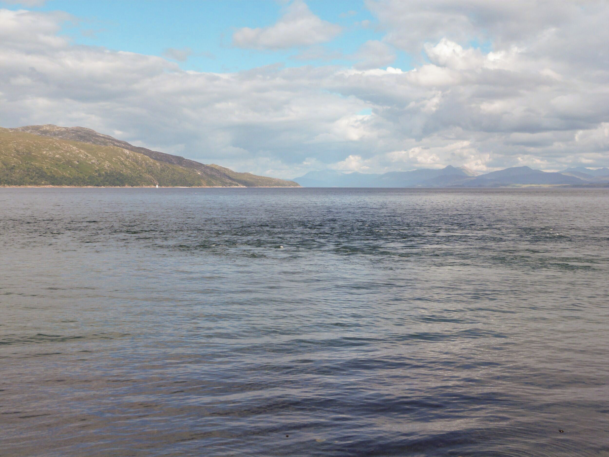 A calm sea with distant mountains and a cloudy sky.
