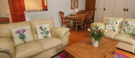 Una sala de estar con dos sofás beige, una mesa de centro de madera y una zona de comedor con sillas y una mesa de madera.