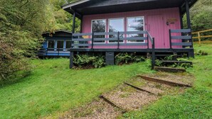A small, single-story cabin with a wooden deck and a covered porch. - Lodge 5 - "hawthorn" (Isle of Arran)