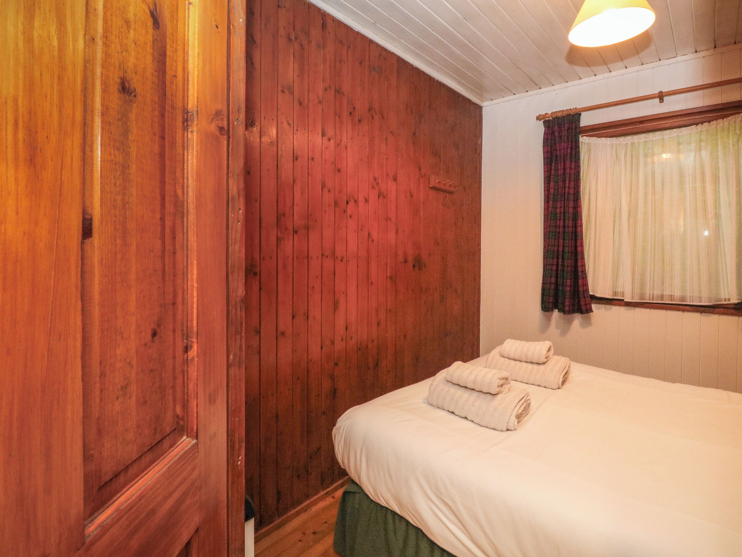 Una habitación con paredes de madera, una cama con ropa de cama blanca y una ventana con cortinas translúcidas.