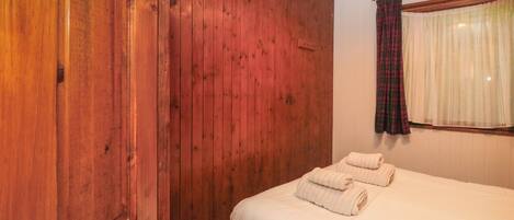 Una habitación con paredes de madera, una cama con ropa de cama blanca y una ventana con cortinas translúcidas.