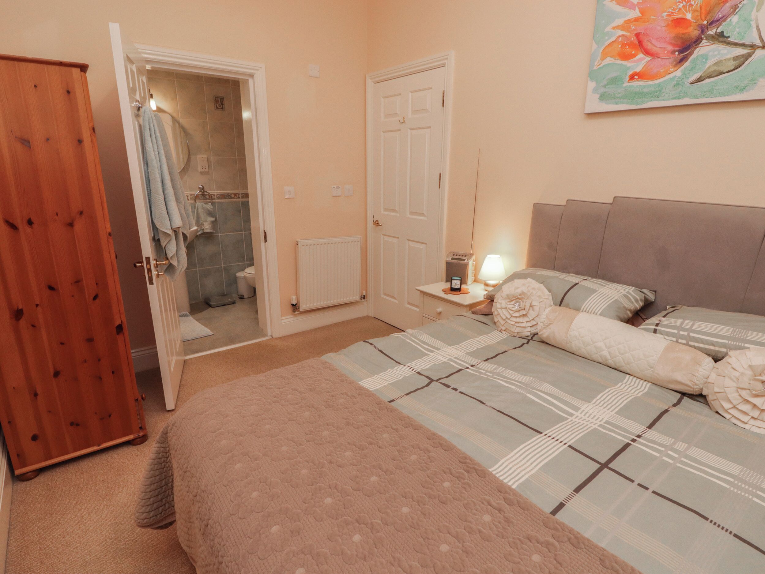 A bedroom with a bed, a nightstand, a wooden wardrobe, and a bathroom visible through an open door.