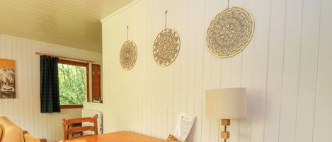 Una mesa de comedor de madera con sillas, una lámpara y adornos en la pared, todo en una habitación con paneles blancos.