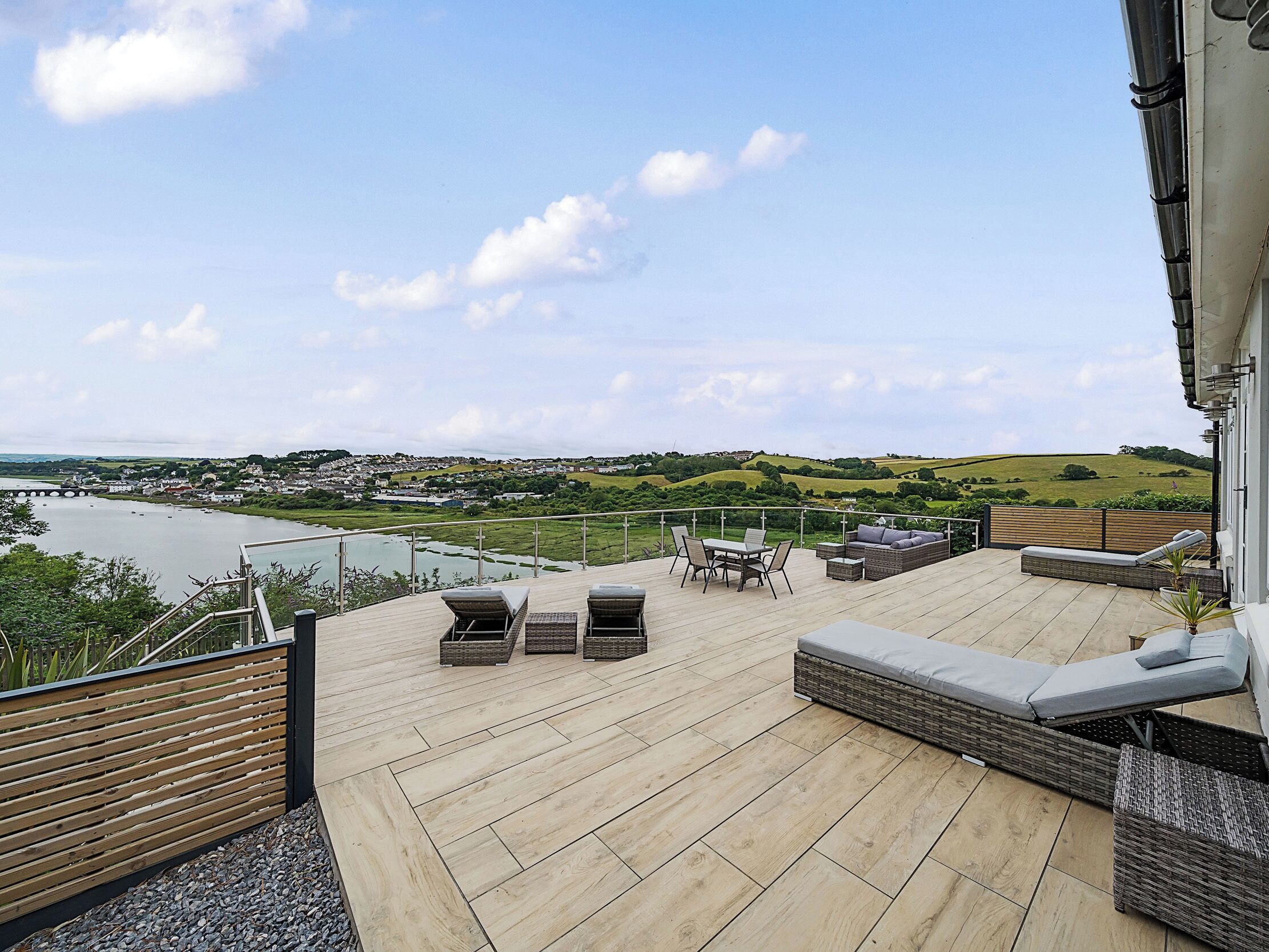 A wooden deck with outdoor furniture, overlooking a river and a town.