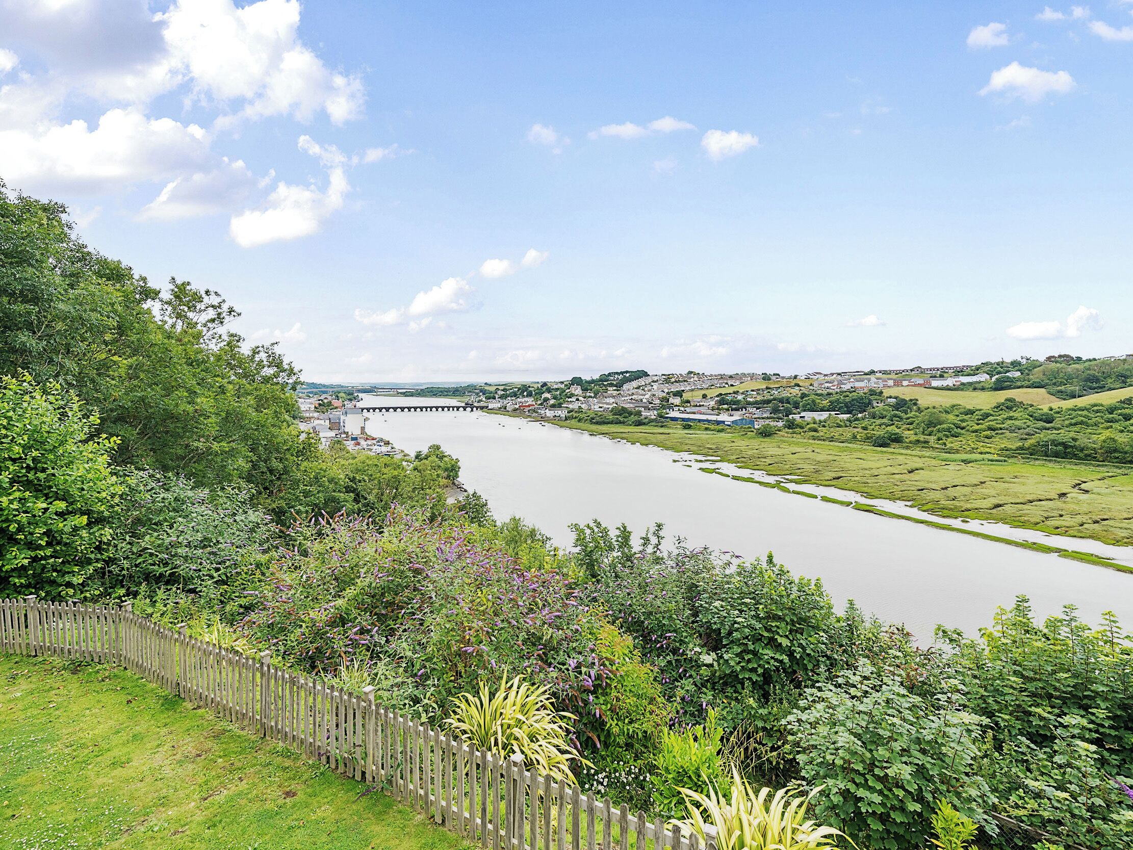 A river with a bridge, surrounded by greenery and a wooden fence.
