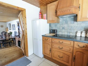 A kitchen with wooden cabinets, a white refrigerator, a tiled backsplash, and a dining area with a table and chairs.