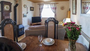A cozy living room with a wooden ceiling, a television, a sofa, and a dining table set for two.